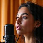 Sofía Montoya cantando apasionadamente en un micrófono de estudio, con una iluminación suave que resalta su presencia.